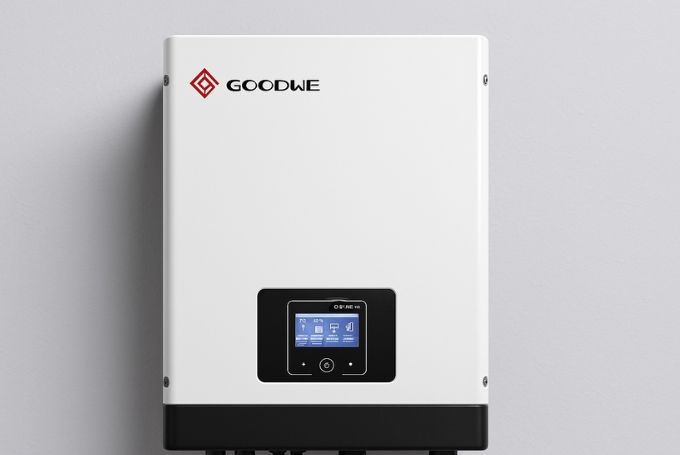 Horizontal hyper-realistic GoodWe GW5000 EM on-grid solar inverter with white casing, red GoodWe logo, LCD display, and black base connectors mounted on a clean gray wall.
